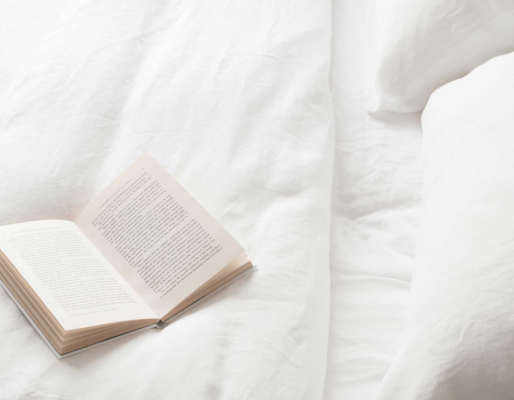 White linen duvet cover, sheet and pillowcases on bed with open book