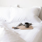 White Egyptian cotton bedlinen showing sheet and pillow detail with duvet cover pulled back and a mug on the bed. Scooms