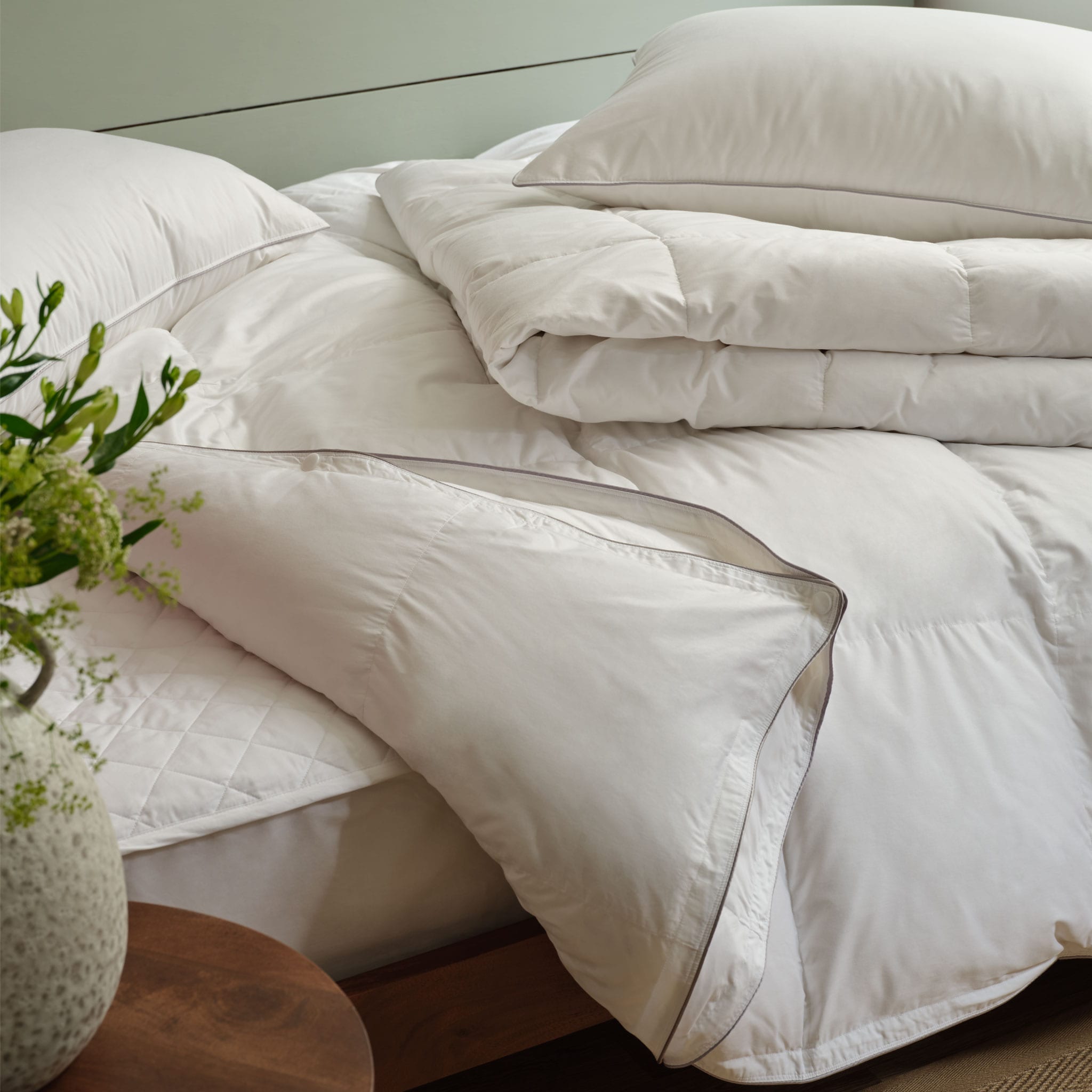 Duvet on a bed folded back to show a cotton mattress protector. Scooms
