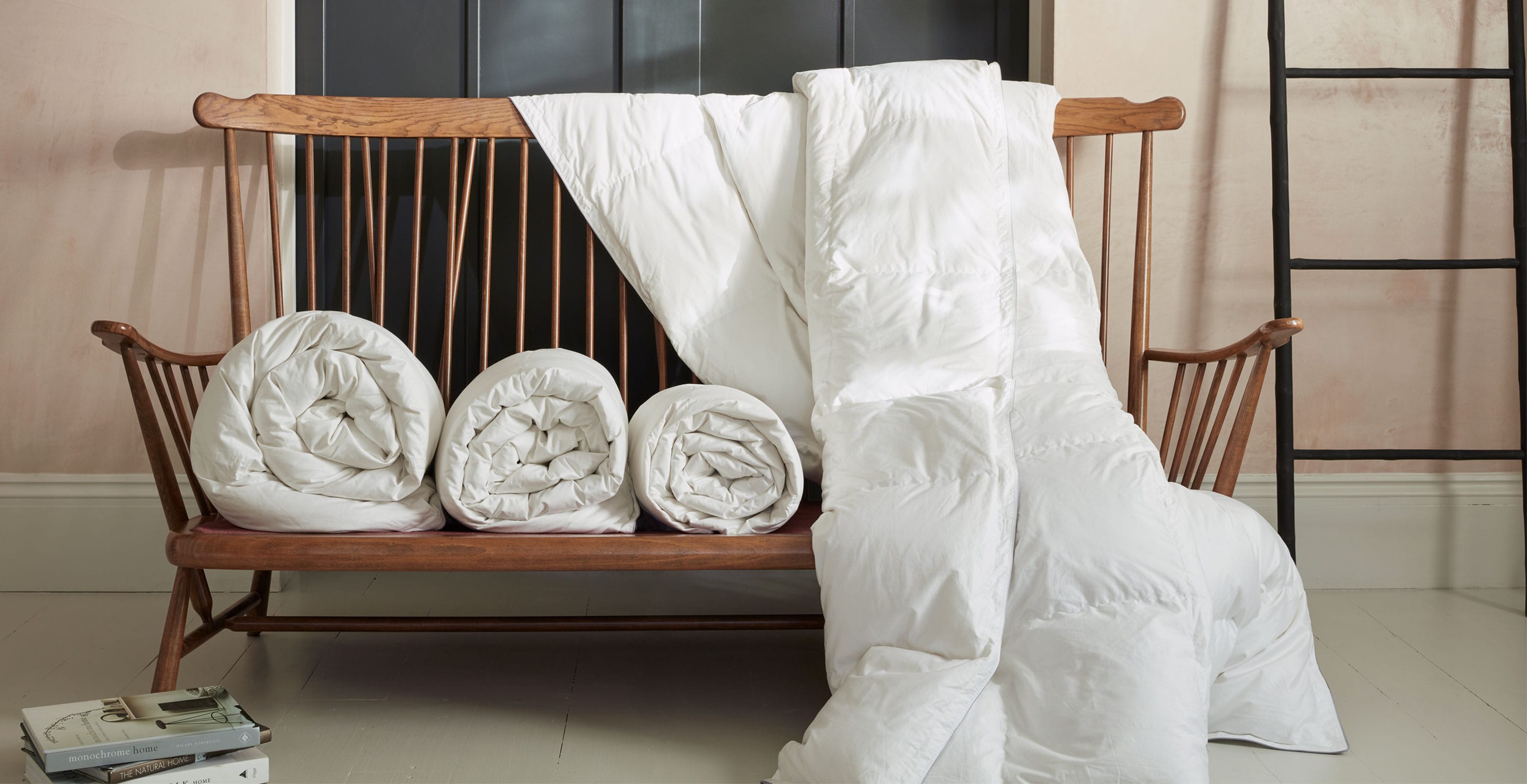 Rolled and draped Hungarian goose down duvets on a wooden bench seat. Scooms