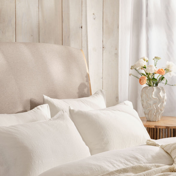 Light and airy bedroom with bed made with white linen bedding. Scooms