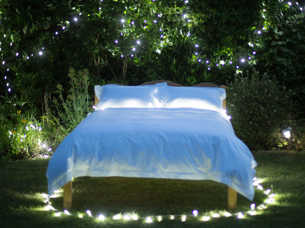 Made Bed in a Garden at Night Surrounded by Lights | scooms