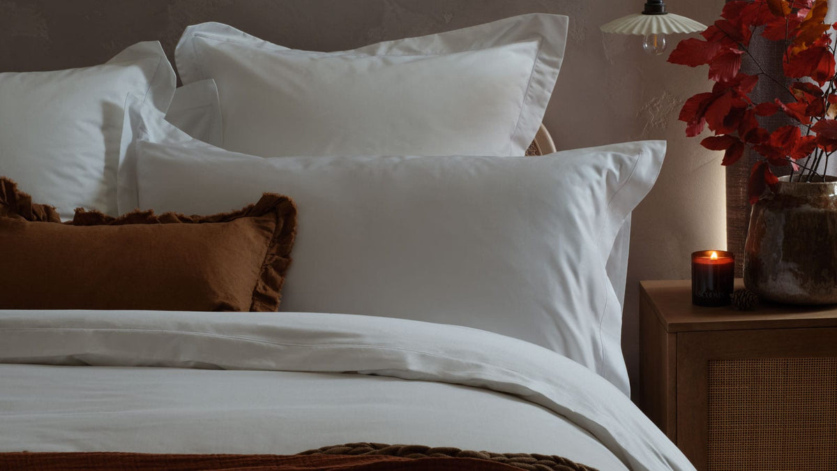 White bedding on a made bed with a candle and foliage in red and brown tones