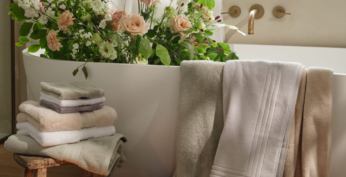 Bathtub with flowers and range of towels in white, green, cream and grey draped over the bath and piled on a stool. | Scooms