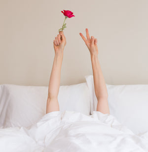 Person In Bed With Their Arms in The Air Holding a Rose | scooms