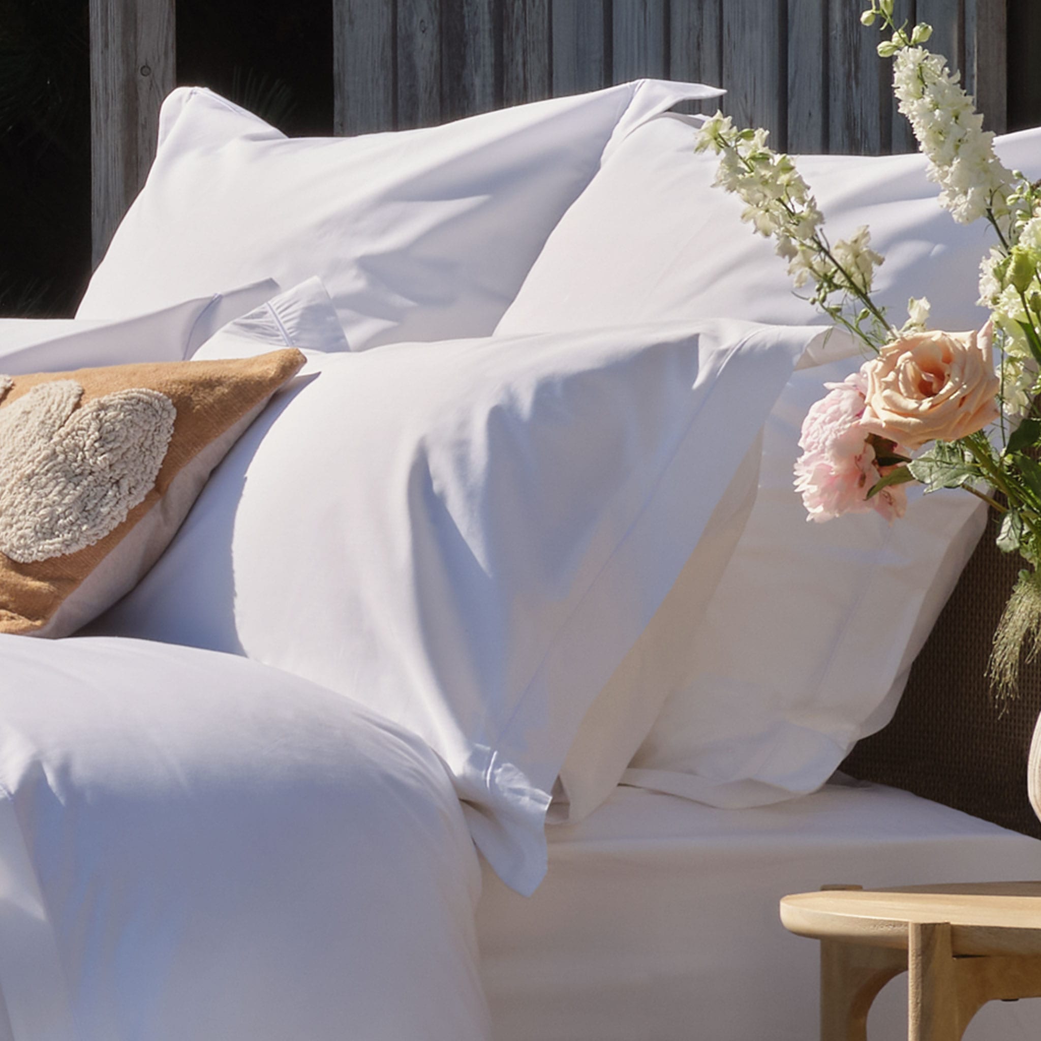 Percale cotton sheets, duvet cover and pillowcases on a bed with a vase of flowers on a side table | Scooms