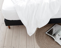 White Egyptian cotton sheets draped over bed with wooden floor and architectural magazine