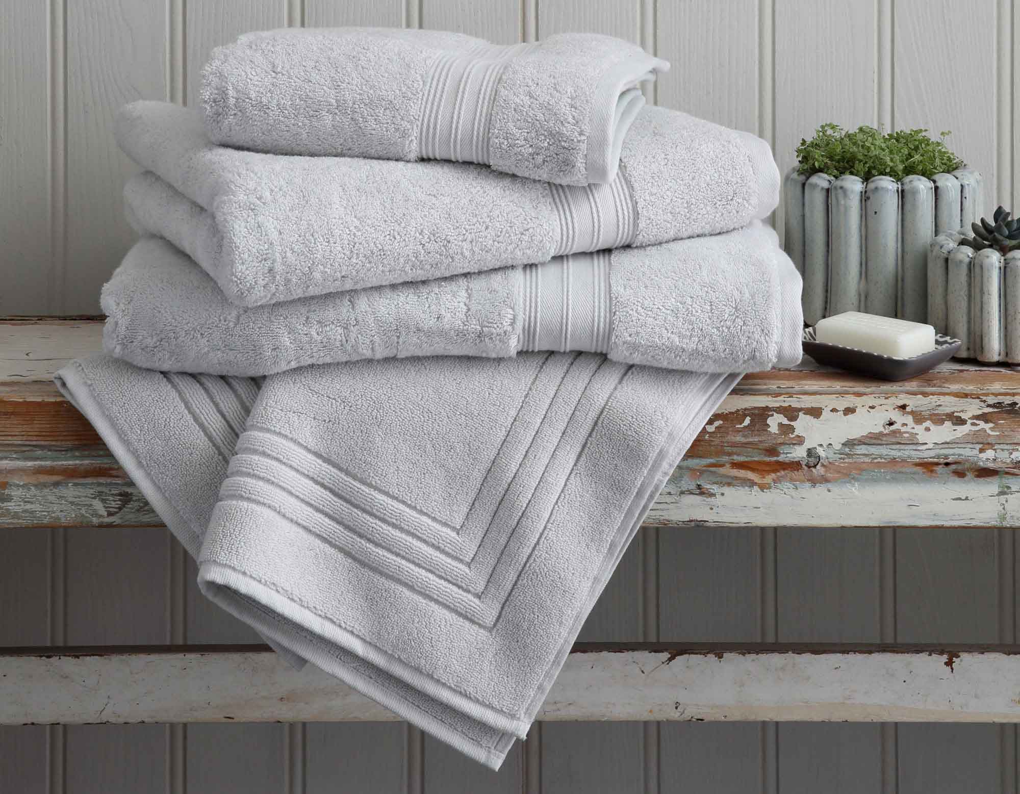 Bundle of pearl grey bath towels and bath mat on rustic bench with soap and grey vases