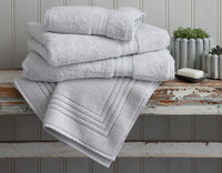 Bath towels and bath mat on rustic bench with soap and grey vases