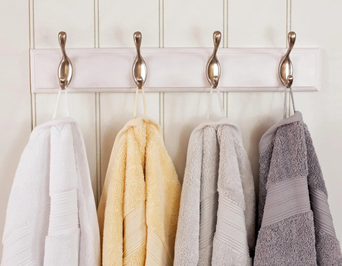 White, Silver Grey, Pearl Grey And Creme Cotton Bath Towels Hanging from Hooks on Wall