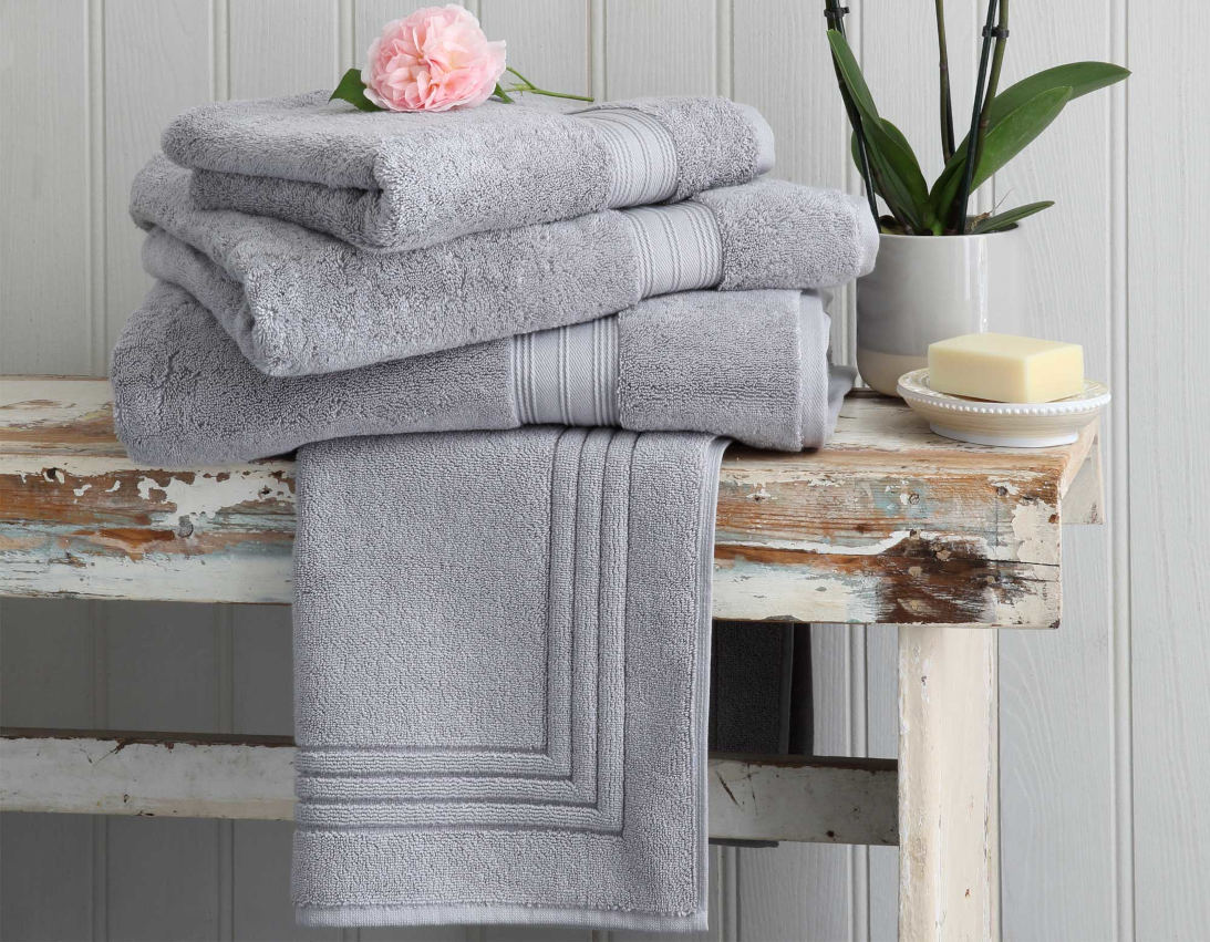 Bundle of silver grey bath towels on rustic bench with flower and soap accessories