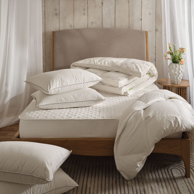 Down pillows, topper and duvet on a bed with a mattress protector. In a light and airy bedroom with net drapes. Scooms