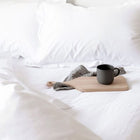 Egyptian cotton bedding in white with the duvet pulled back and a coffee mug and tray in the bed. Scooms