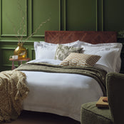 Egyptian cotton bedding in white on a made bed in a luxurious bedroom. Scooms