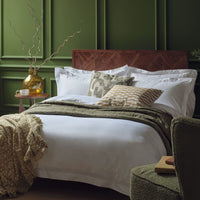 Egyptian cotton bedding in white on a made bed in a luxurious bedroom. Scooms