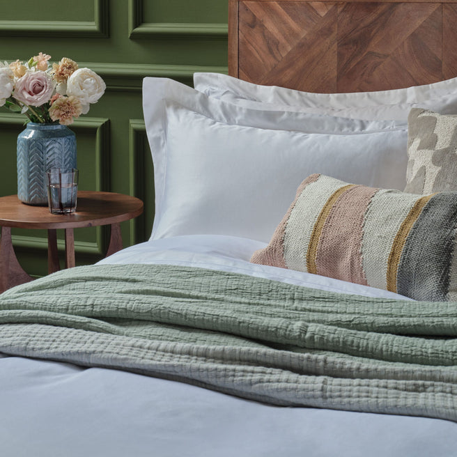 Bed with white Egyptian cotton pillowcases and duvet cover and a green blanket, side table with flowers and water glasses. Scooms