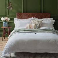 Bedroom with a wooden headboard, white Egyptian cotton bedding and pillows against a green panelled wall.