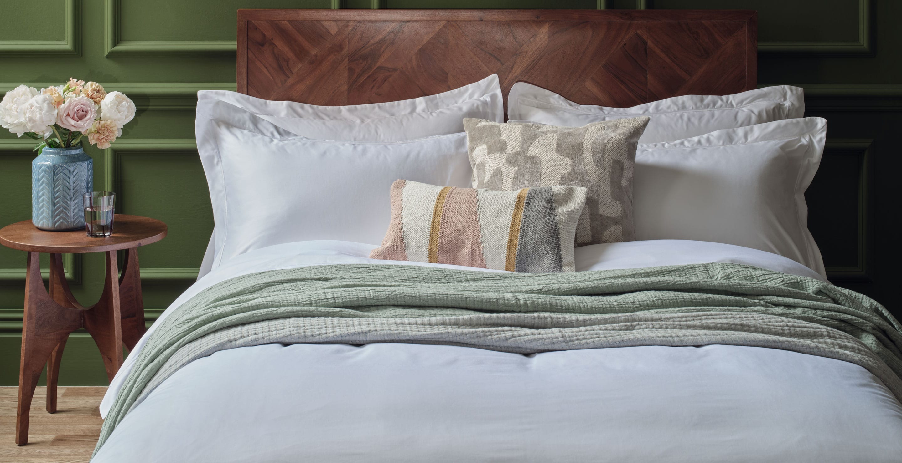 Bed with Scooms white bedding, decorative pillows, and a wooden headboard against a green wall.