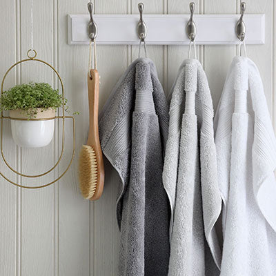 Grey and white Egyptian cotton towels hanging in a bathroom with a scrubber. Scooms