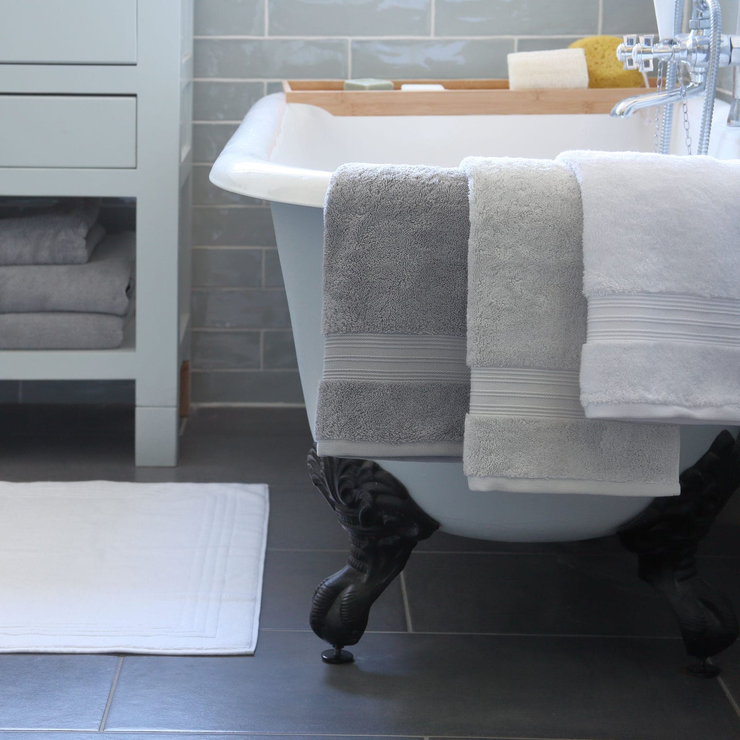 White and grey Egyptian cotton towels draped over a white bath tub in a bathroom. Scooms