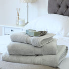 Bundle of pearl grey Egyptian cotton bath towels and hand towels on a bed. Scooms 