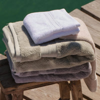 A stack of folded bath towels in natural, green, cream and white tones, displayed on a rustic wooden stool. | Scooms