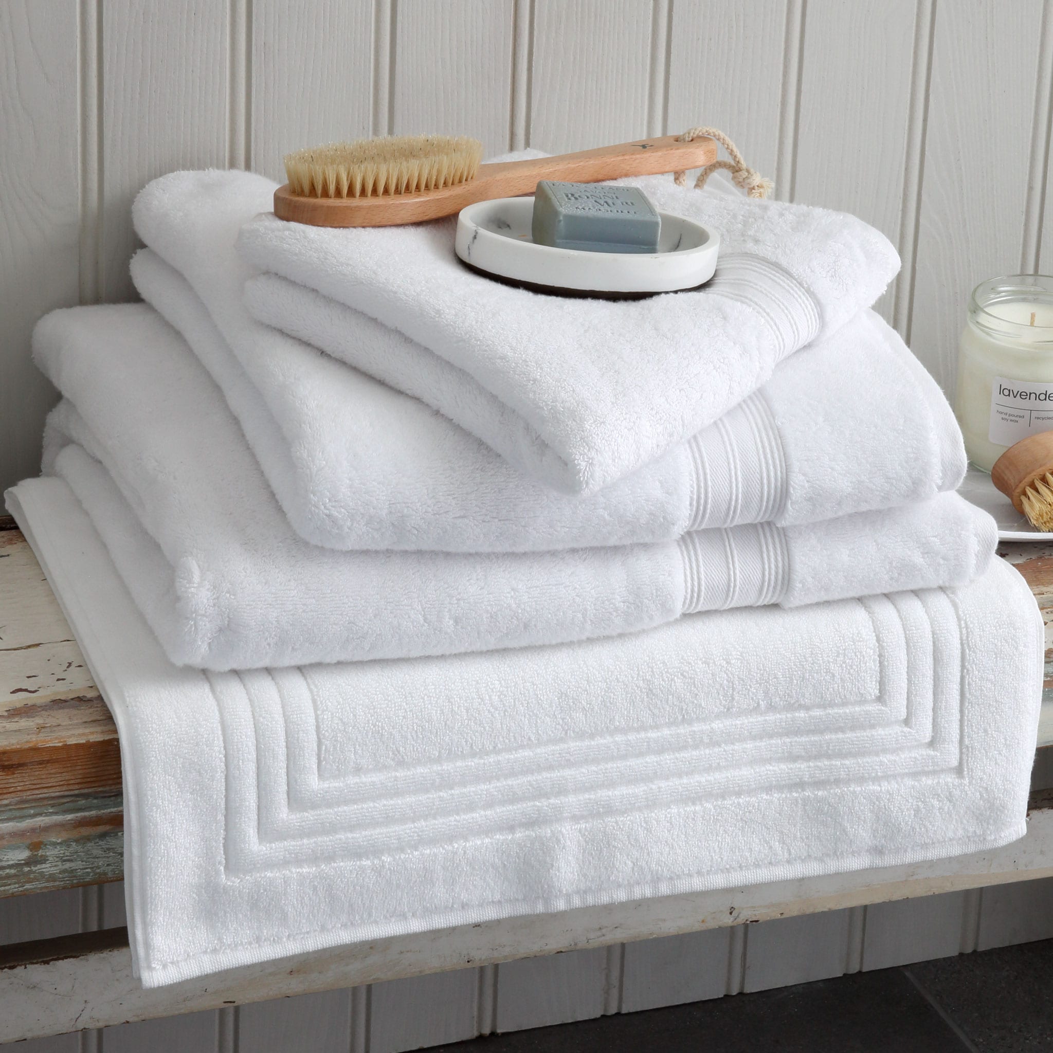 Pile of white Egyptian cotton towels and a bath mat on a wooden bench