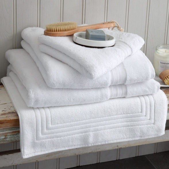 Pile of white Egyptian cotton towels and a bath mat on a wooden bench