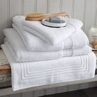 Bundle of white Egyptian cotton towels, bath mat and face cloth on a wooden bench. Scooms
