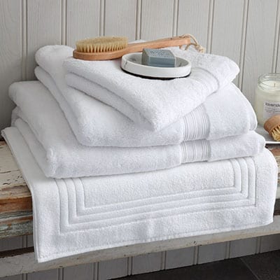 Bundle of white Egyptian cotton towels, bath mat and face cloth on a wooden bench. Scooms