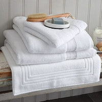 Bundle of white Egyptian cotton towels, bath mat and face cloth on a wooden bench. Scooms