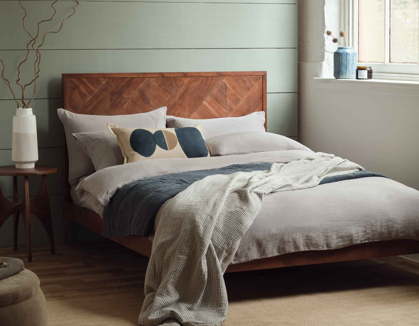 Grey linen bedding on a bed with a wooden headboard
