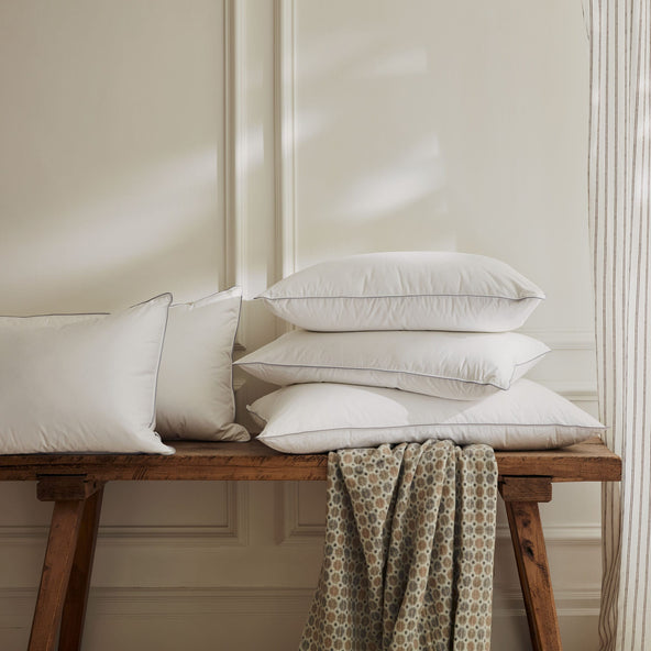 Hungarian goose down pillows on a wooden bench next a window with drapes and a dappled light. | Scooms