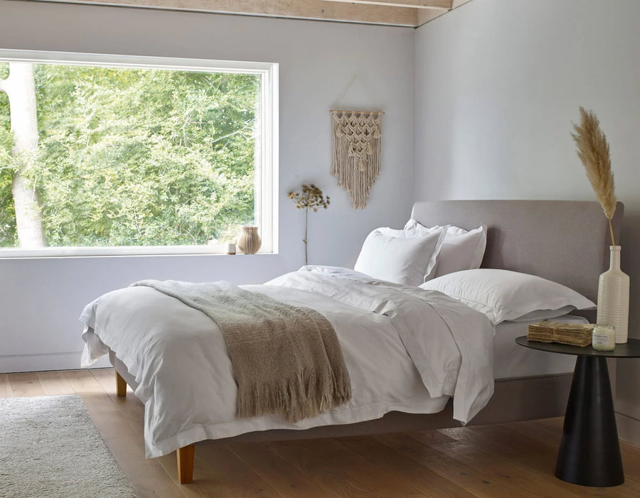 White Egyptian cotton kingsize fitted sheet on bed with duvet draped over bed wooden floor and architectural magazine