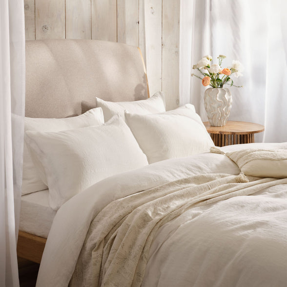 Light and airy bedroom with bed made with white linen bedding. Scooms