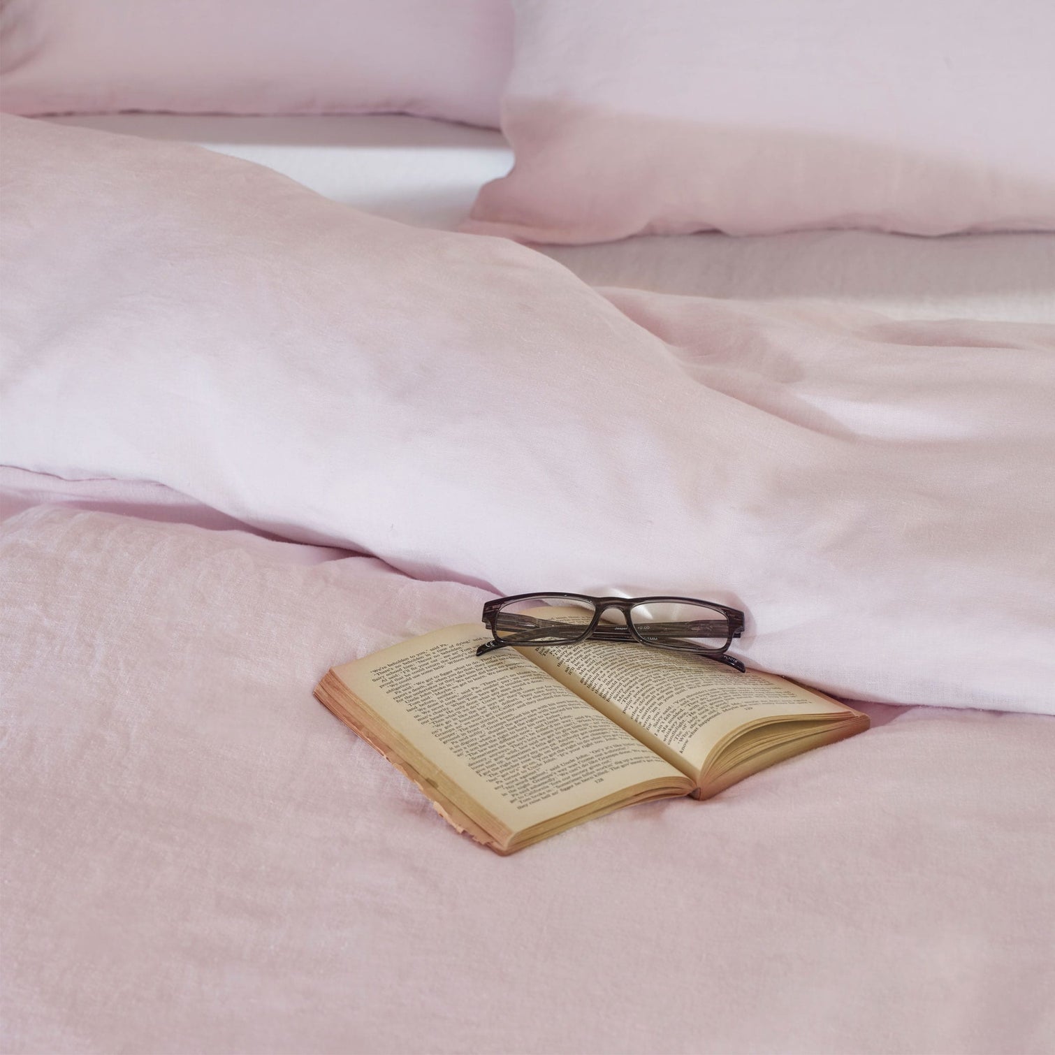 Pink linen bedding on a bed with a book and glasses. Scooms