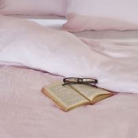 Pink linen bedding on a bed with a book and glasses. Scooms