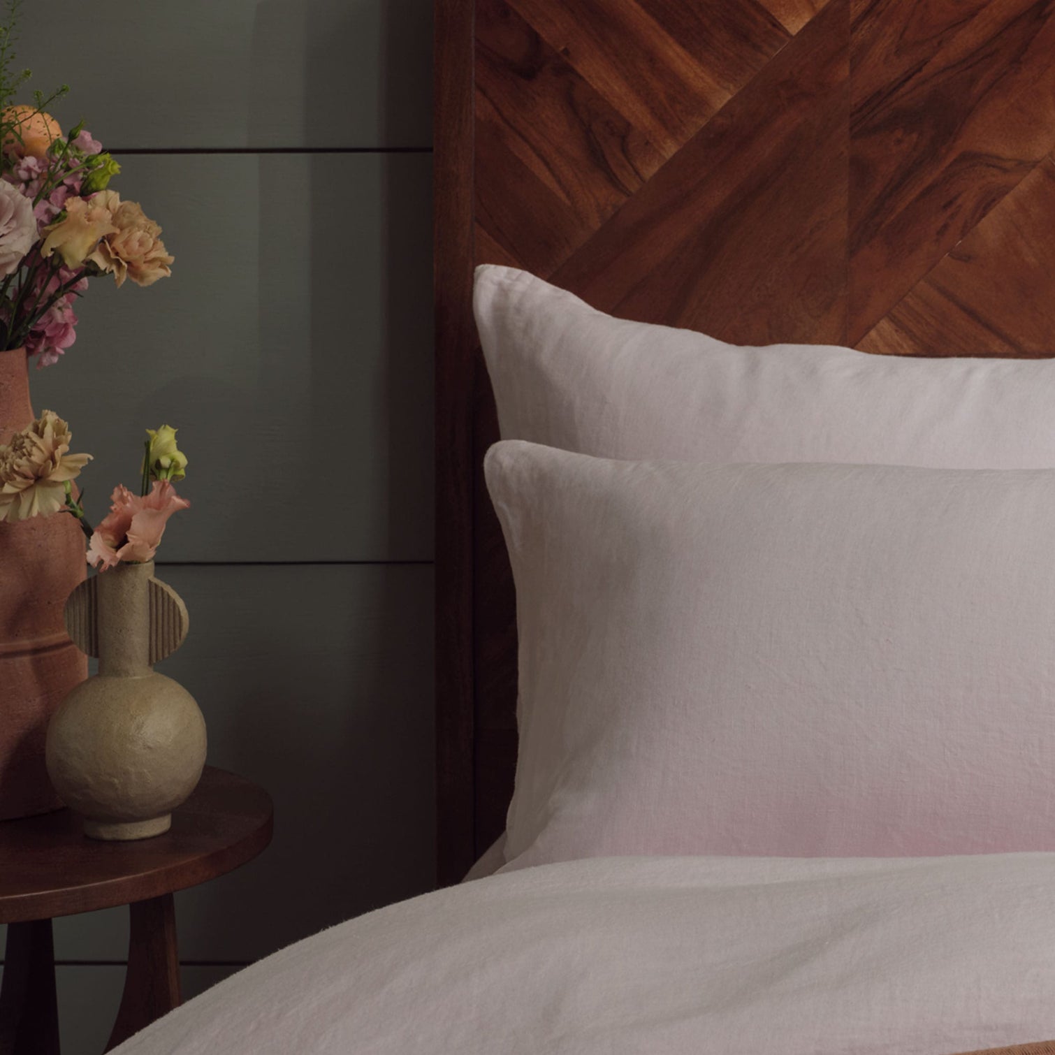 Closeup of pink linen pillowcases on a made bed with a panelled background. Scooms
