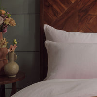 Closeup of pink linen pillowcases on a made bed with a panelled background. Scooms