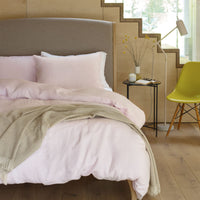 Pink linen bedding on a bed in a scandi style room with a wooden staircase in the background. Scooms