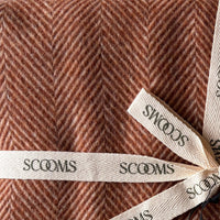 Close-up of a herringbone-patterned coral coloured Merino lambswool throw with 'Scooms' branding.