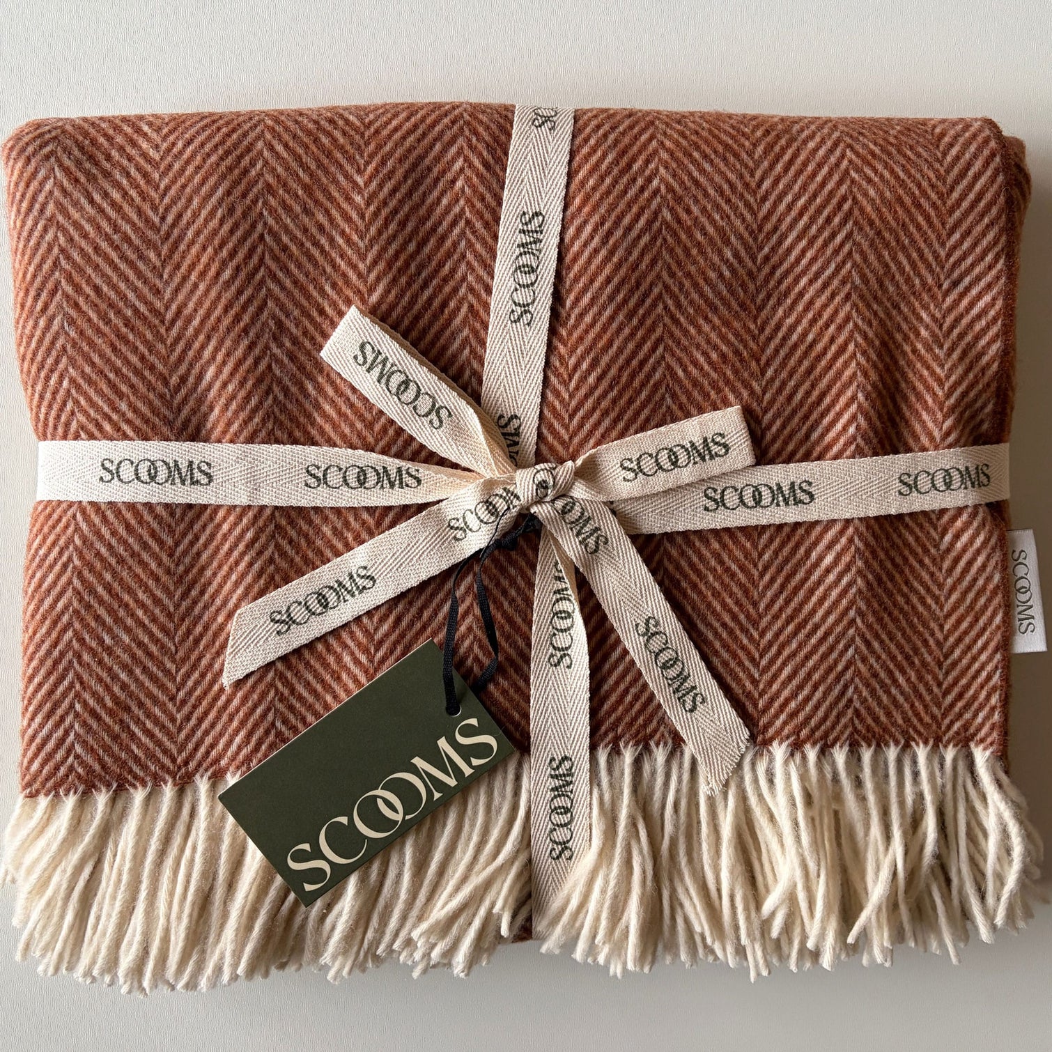 Herringbone-patterned coral Merino lambswool throw with 'Scooms' branding.
