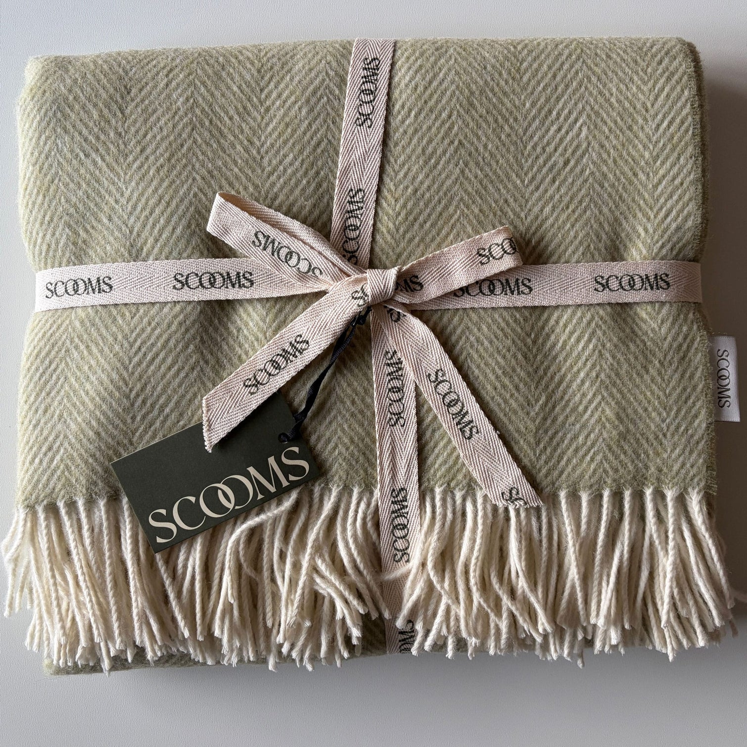 Herringbone-patterned sage green Merino lambswool throw with 'Scooms' branding.