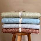 Stack of four folded Merino lambswool throws in different colours on a wooden stool with Scooms branding.