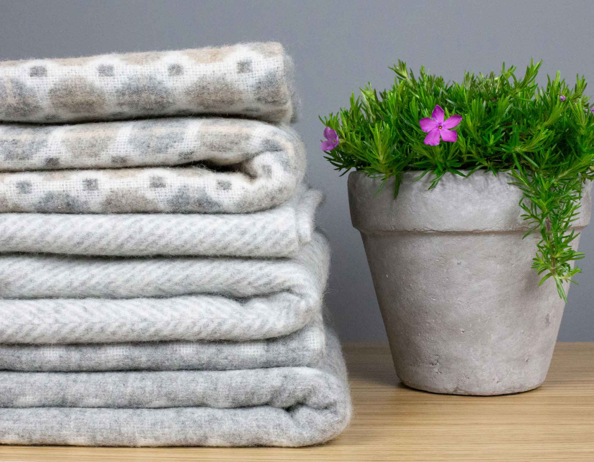 Pile of grey merino wool throws next to plant in a pot