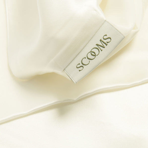 Close-up of ivory silk fitted sheet showing Scooms brand label.