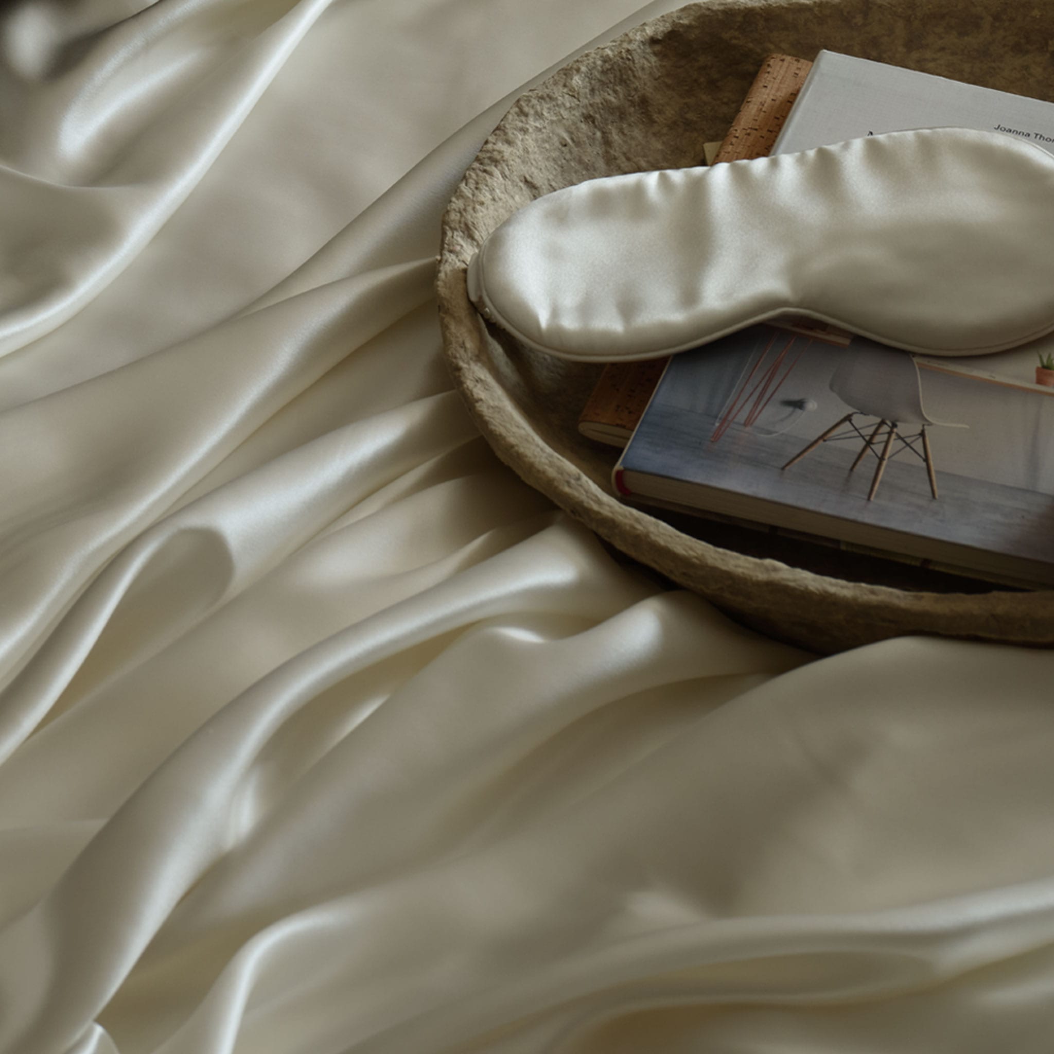 An ivory silk eye mask resting on a tray, on top of a draped ivory Mulberry silk sheet. | Scooms