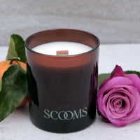 Natural scented candle in an amber glass jar with an orange, rose and leaves | Scooms