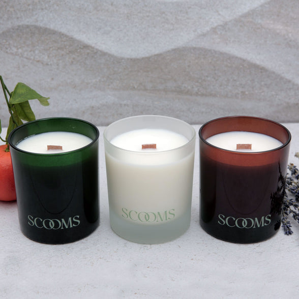 Three natural scented candles in glass jars on a textured surface | Scooms