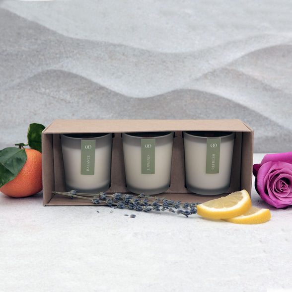 Three natural scented candles in a box set with a lemon, lavender, and rose on a textured surface | Scooms